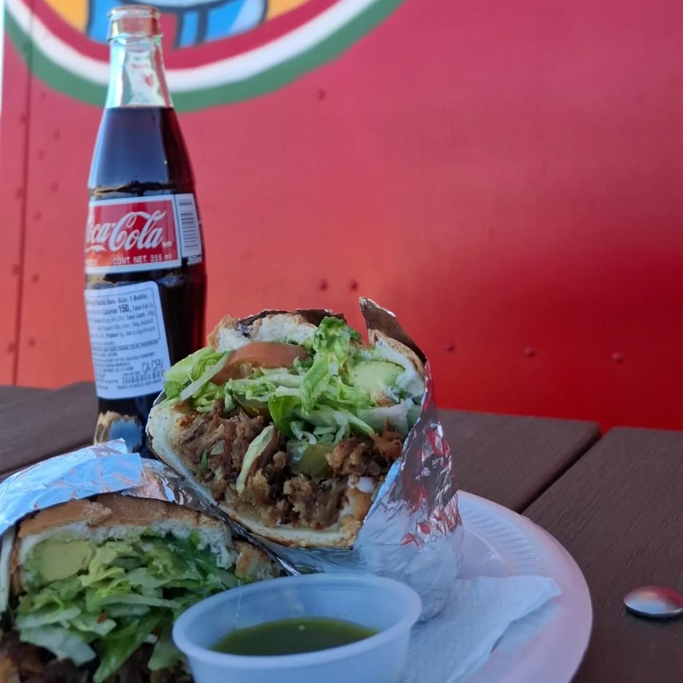 A burrito on a picnic table with a glass bottle of Coca-Cola