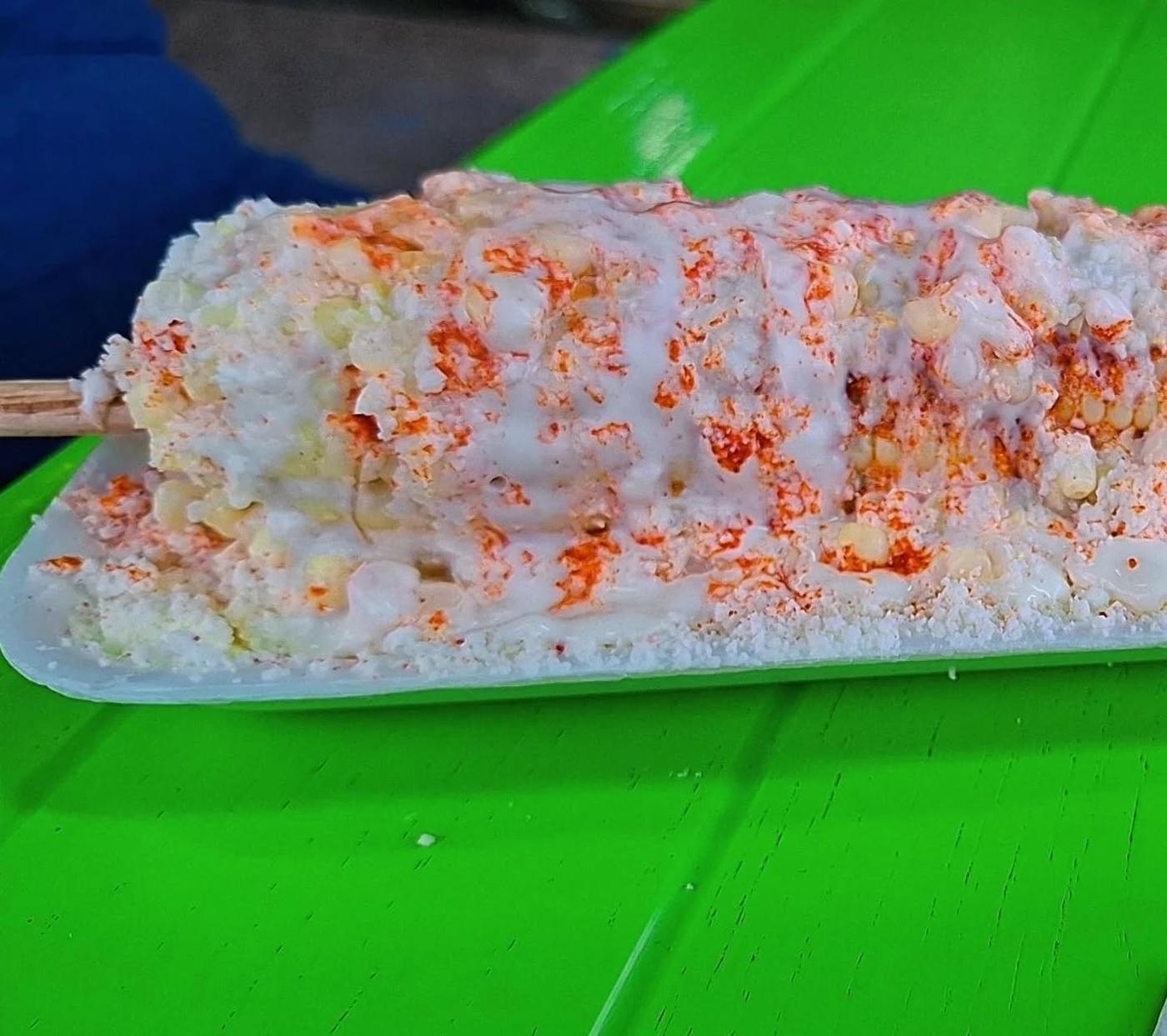 Corn on the cob dressed with mayo, cotija cheese and chili powder on a green table